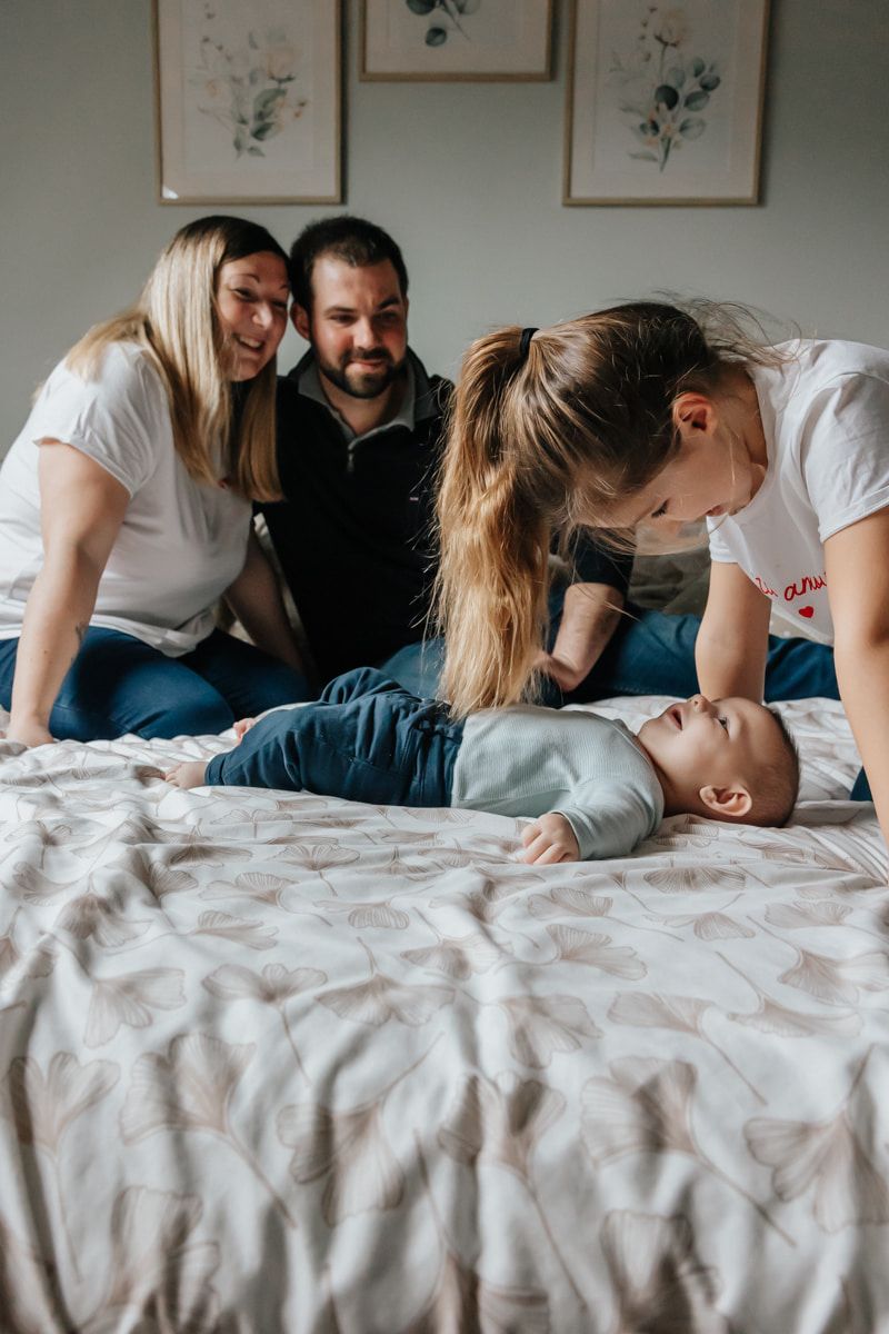 Grande soeur fait rire son petit frere sous le regard attendri de leurs parents, un moment capture par une photographe de famille a Lille