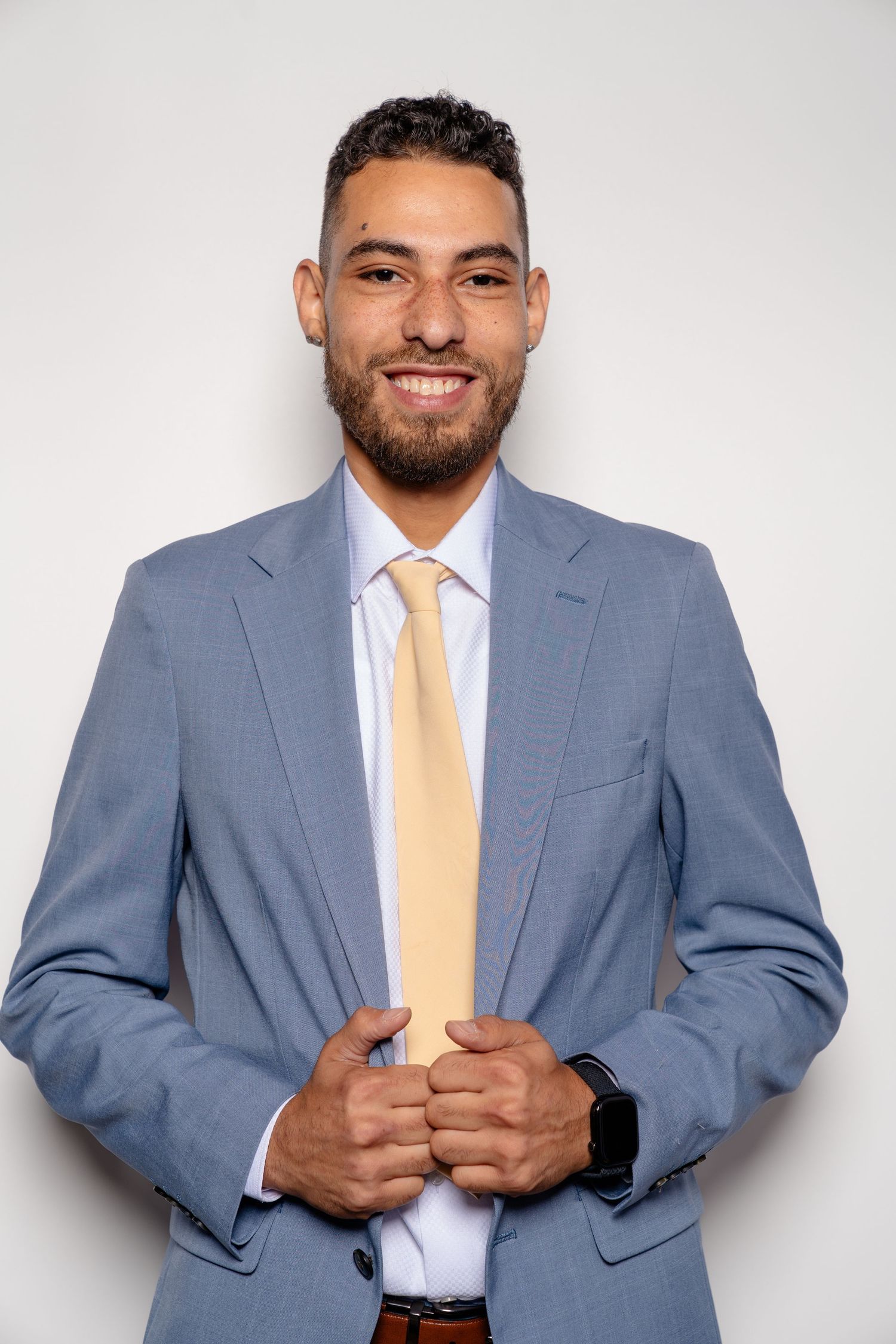 Smiling businessman in blue suit and yellow tie posing confidently against white background.