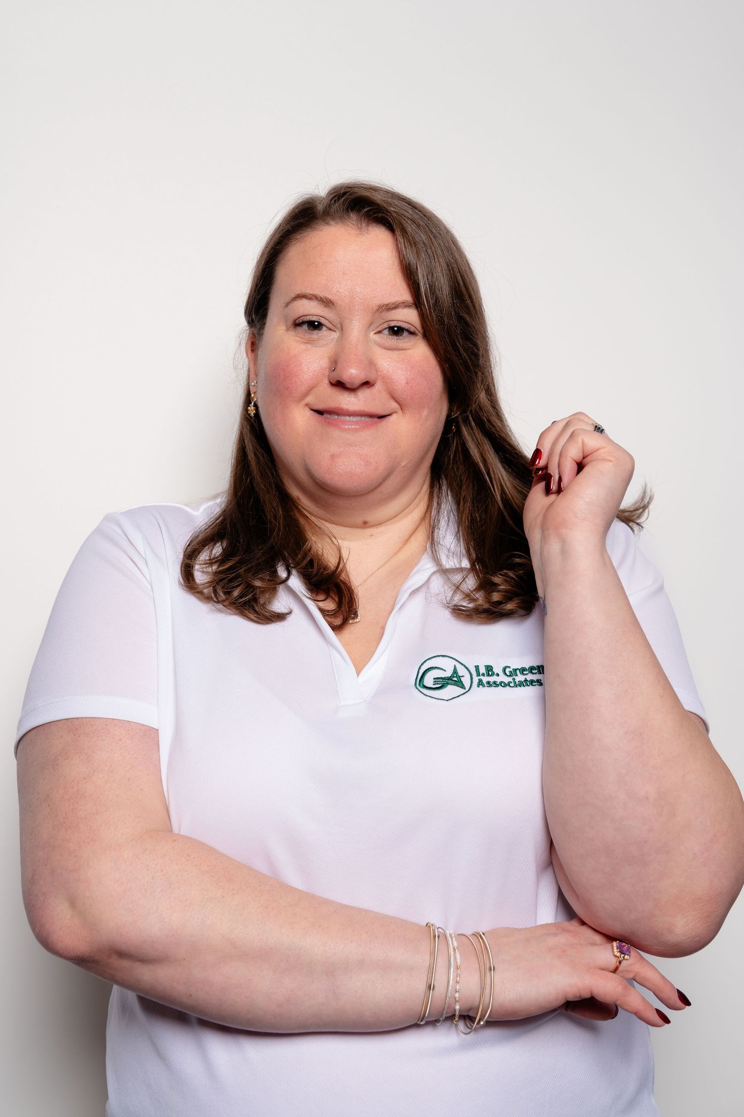 Woman in white L.B. Green Associates polo shirt smiling confidently with arms crossed.