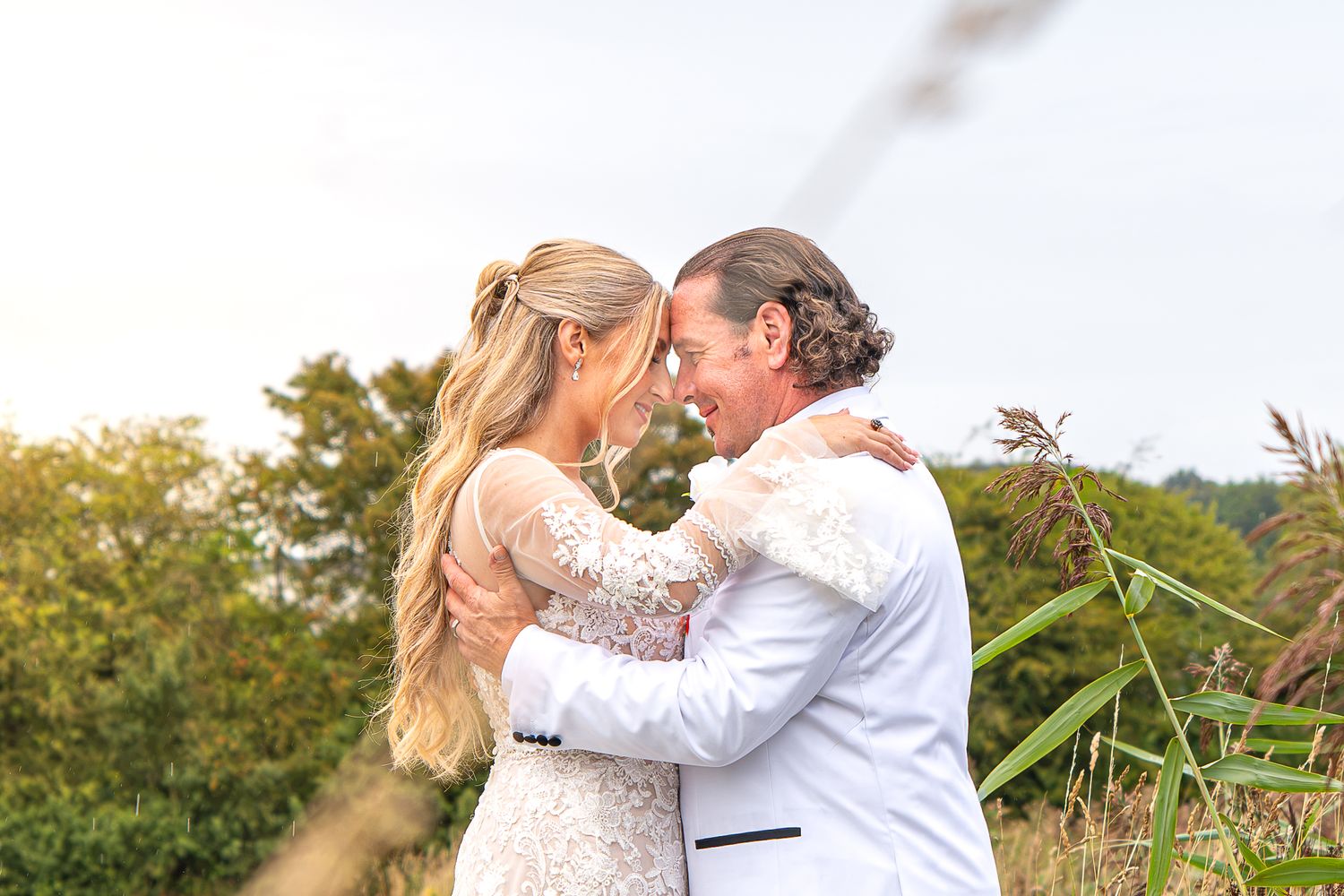 A bride and groom embrace and smile at each other outdoors on their wedding day with lush greenery in the background. Leeds, Yorkshire