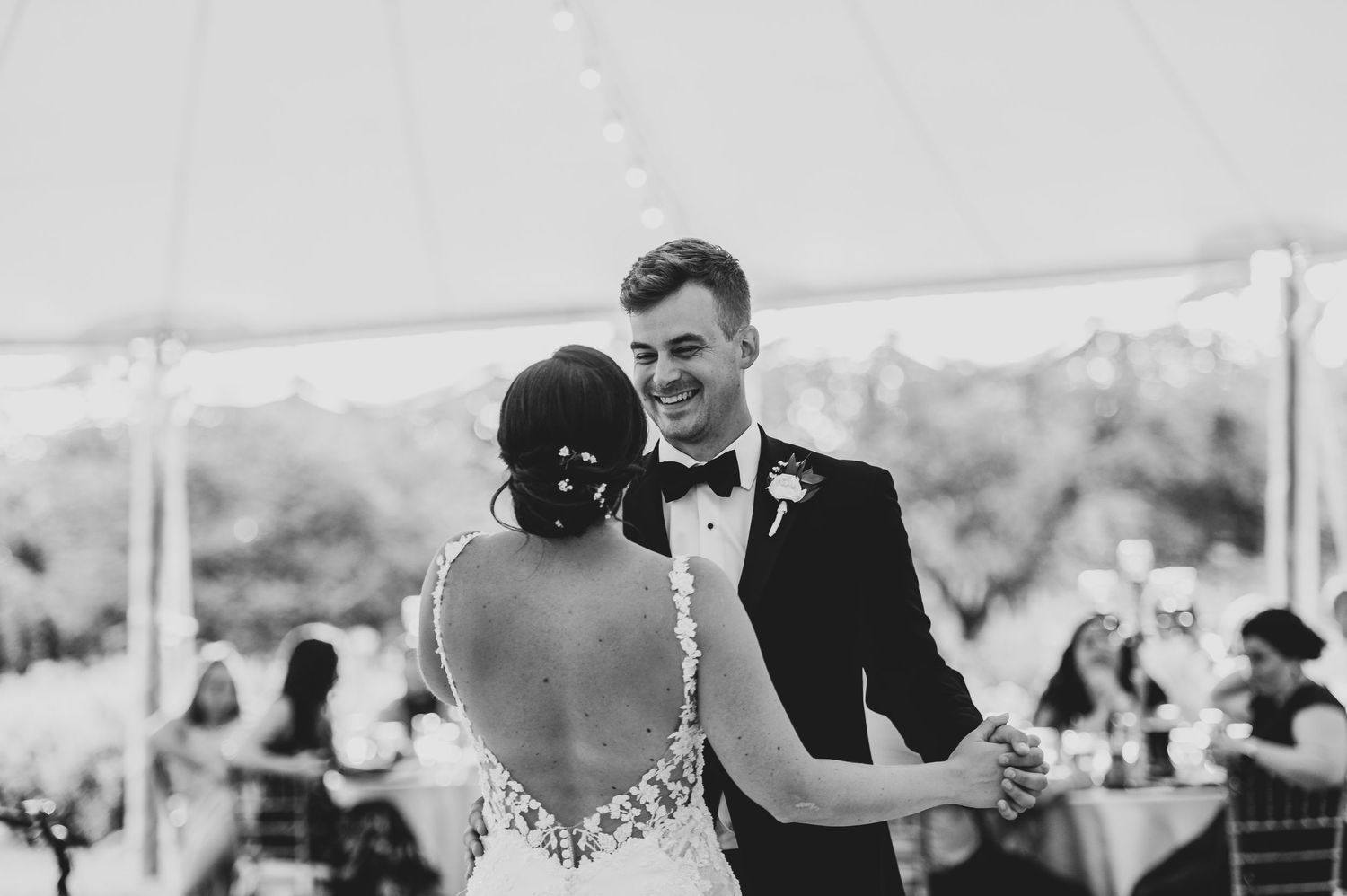 Black and white photo of a couple sharing their first dance at an outdoor tented wedding reception.