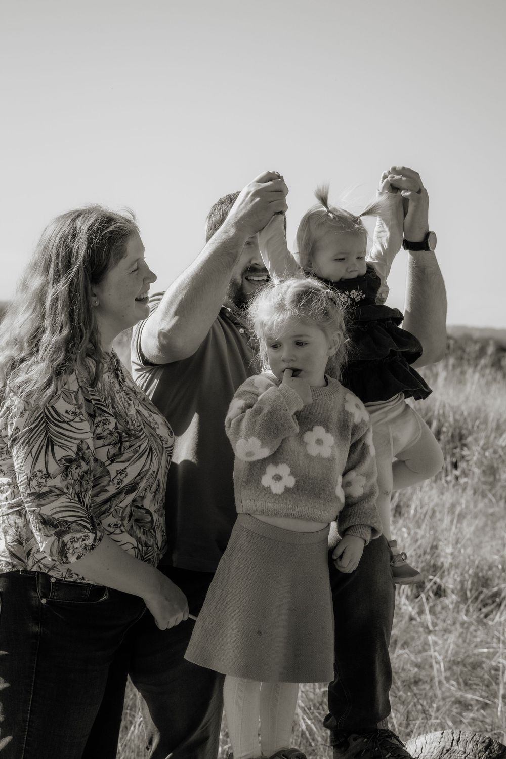 Black and white photo of a happy family with two young children outdoors in a grassy field in Rouse Hill on a sunny day.