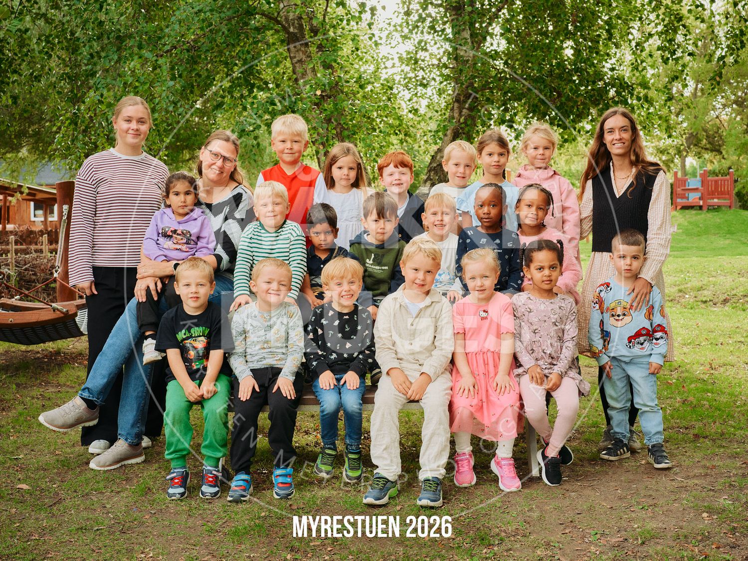Group photo of children and teachers at Myrestuen 2026 kindergarten class, posing outdoors under green trees.