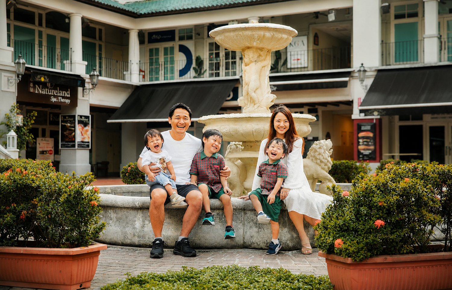 Smiling family of five posing together in front of a decorative stone fountain outdoors.