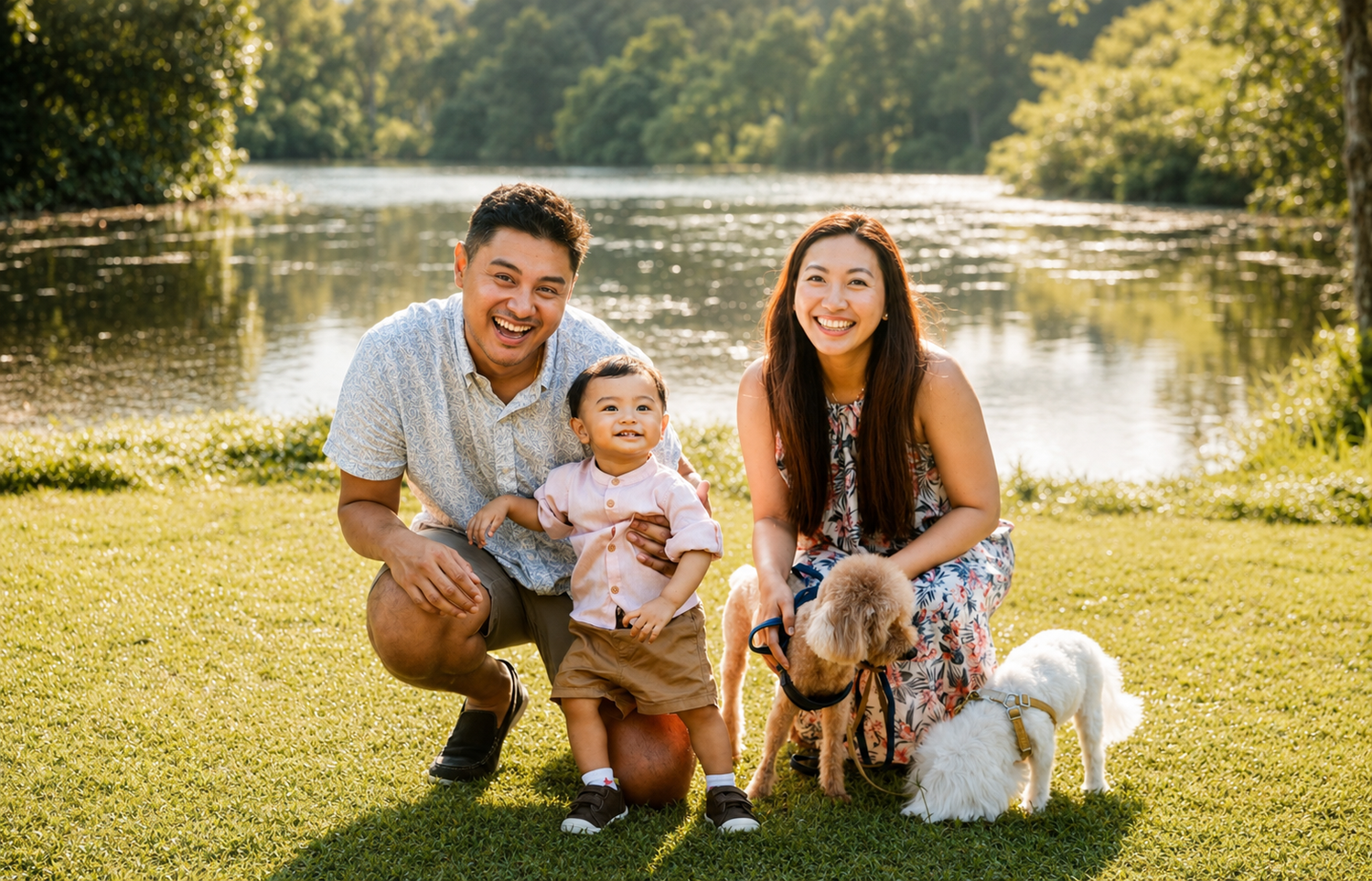 Joyful family with baby and small dogs posing by a sunny lakeside park.