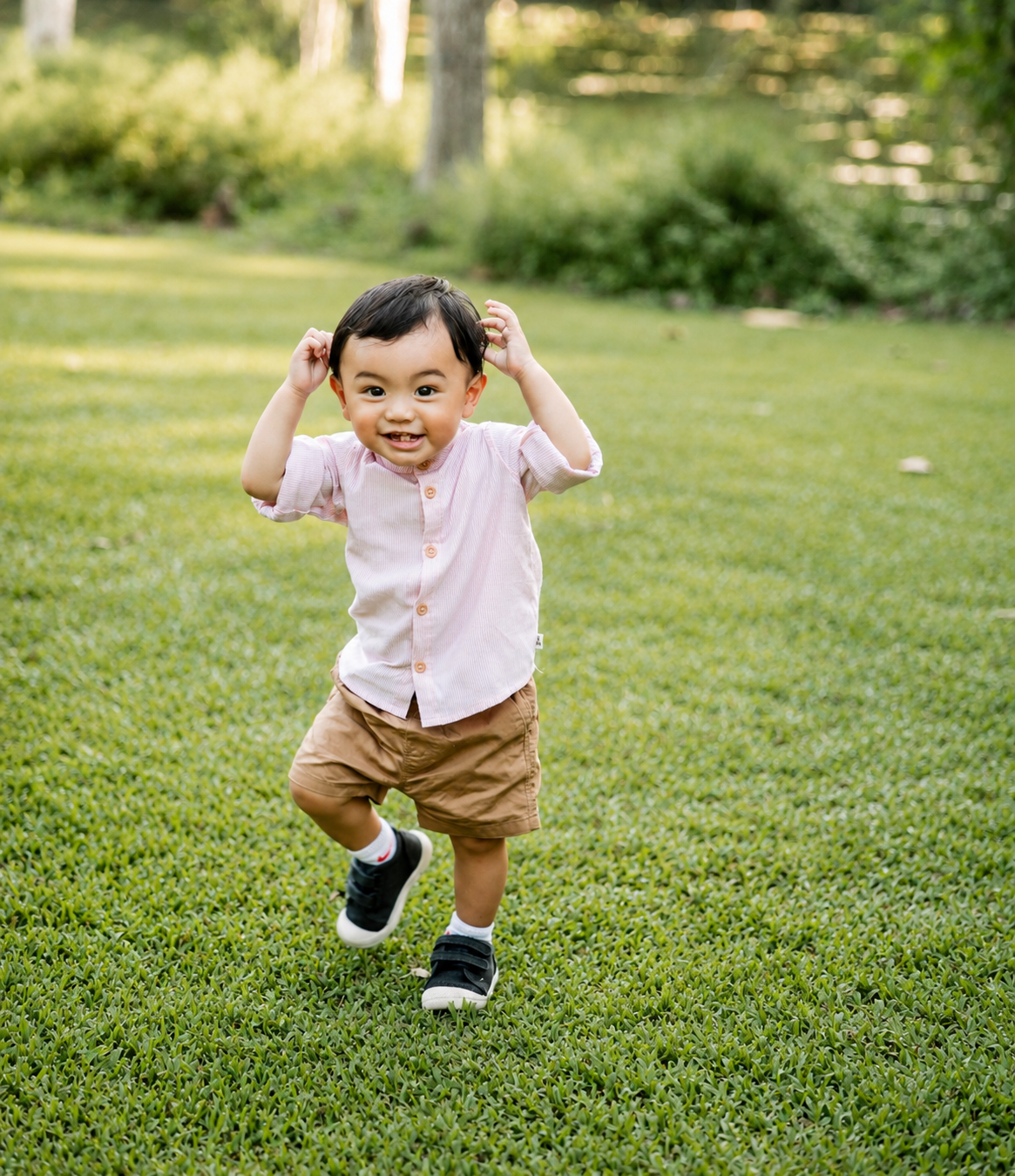 Happy toddler in pink shirt and khaki shorts running on green grass outdoors.