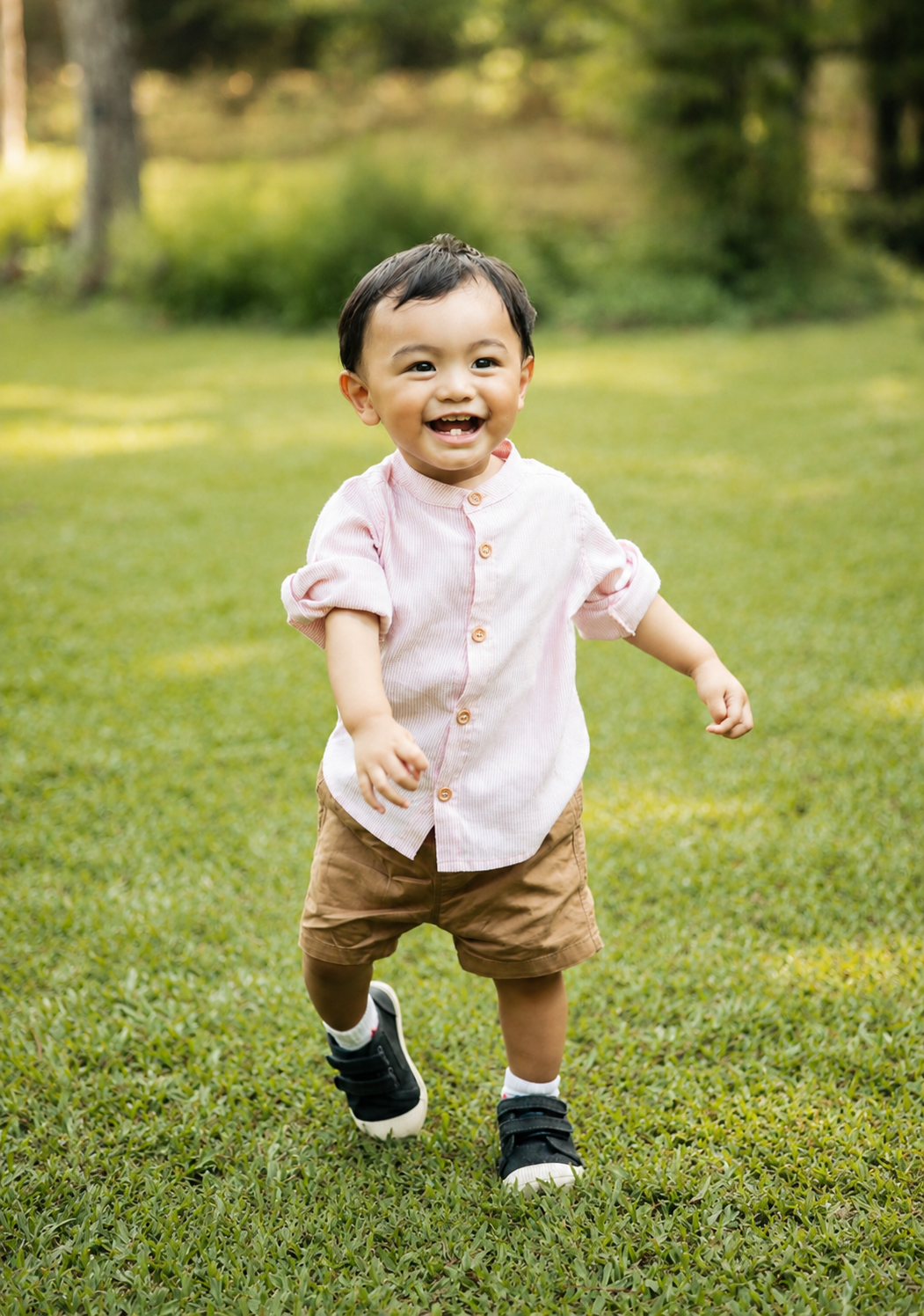 Happy toddler in pink shirt and khaki shorts joyfully running on green lawn.