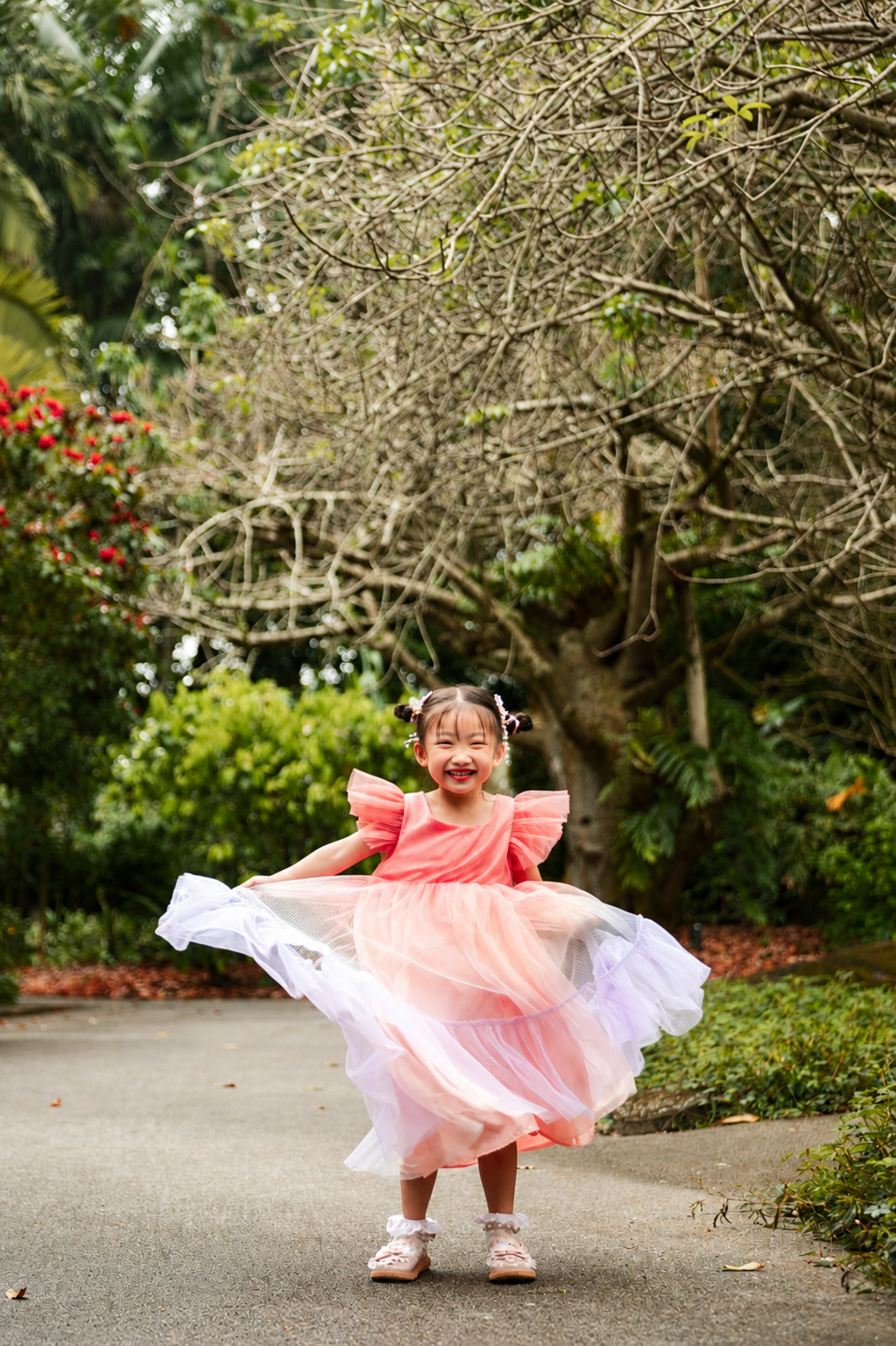Cheerful young girl in pink tulle dress spinning joyfully on a park path surrounded by greenery.