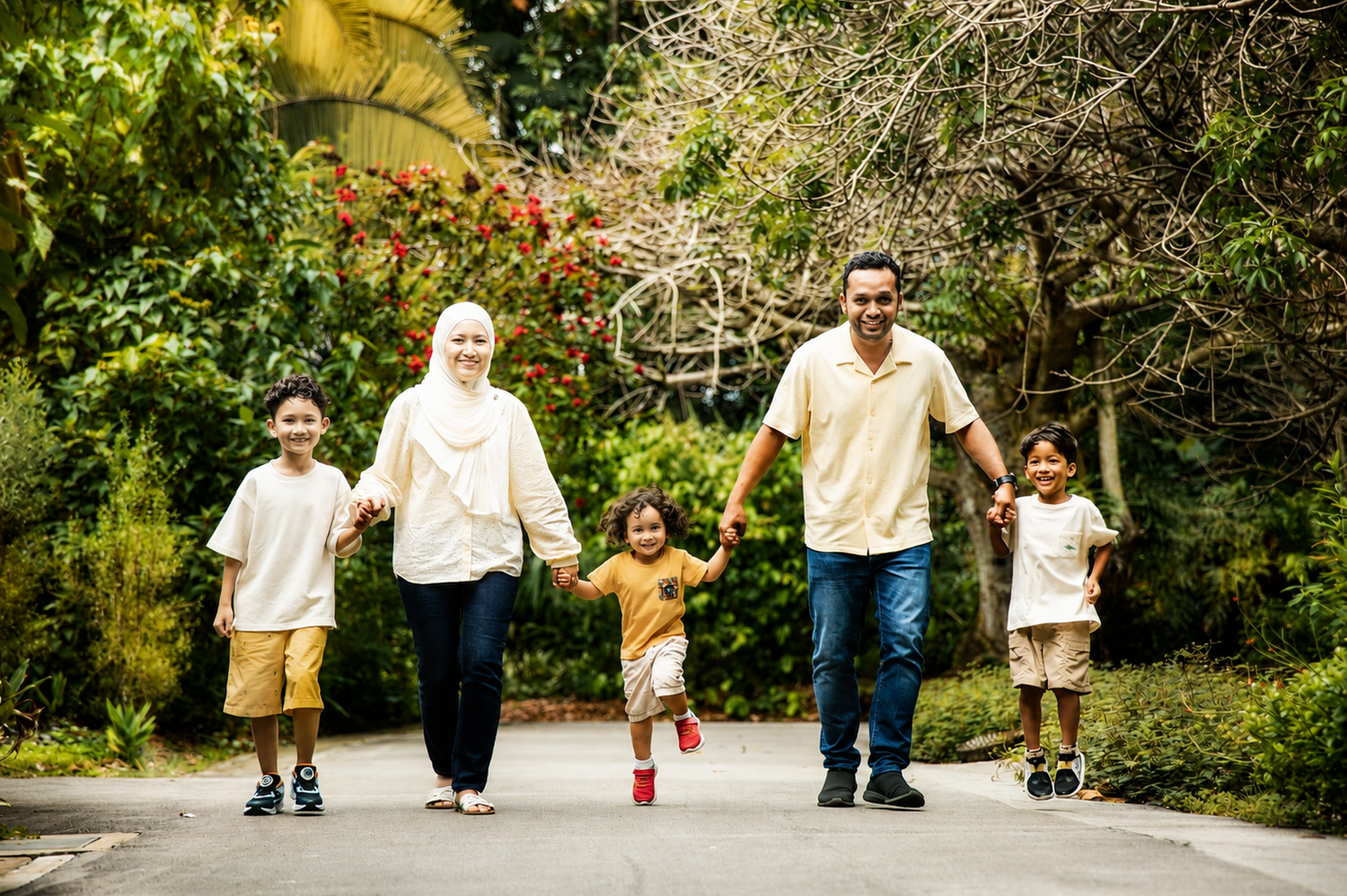 Happy Muslim family of five walking hand-in-hand along a tree-lined garden path together.