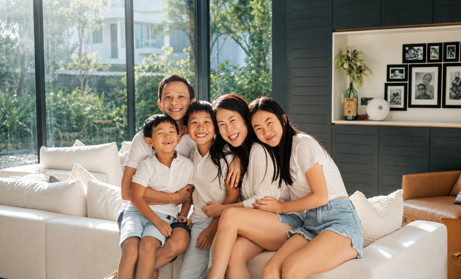 Happy Asian family of five smiling together on a white sofa in a modern bright living room.