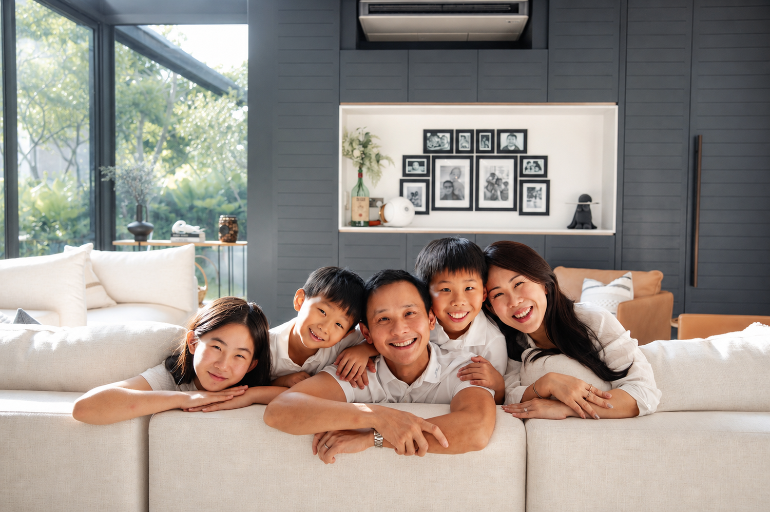 Smiling Asian family of five lying together on a white sofa in a modern living room.
