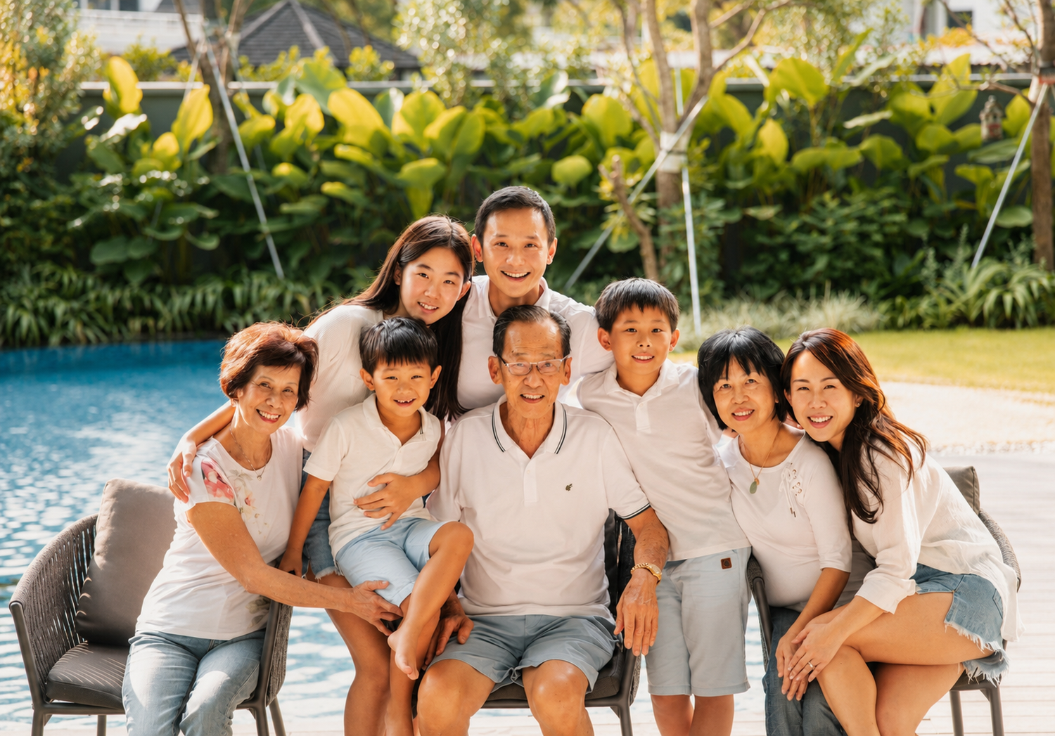 Large happy Asian family posing together outdoors near a swimming pool surrounded by greenery.