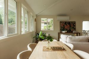 Dining room with a wood table, white chairs, and large windows bringing in natural light.