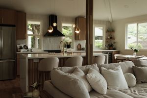 Open-plan family room with a light-colored sofa beside a kitchen with an island and pendant lights.