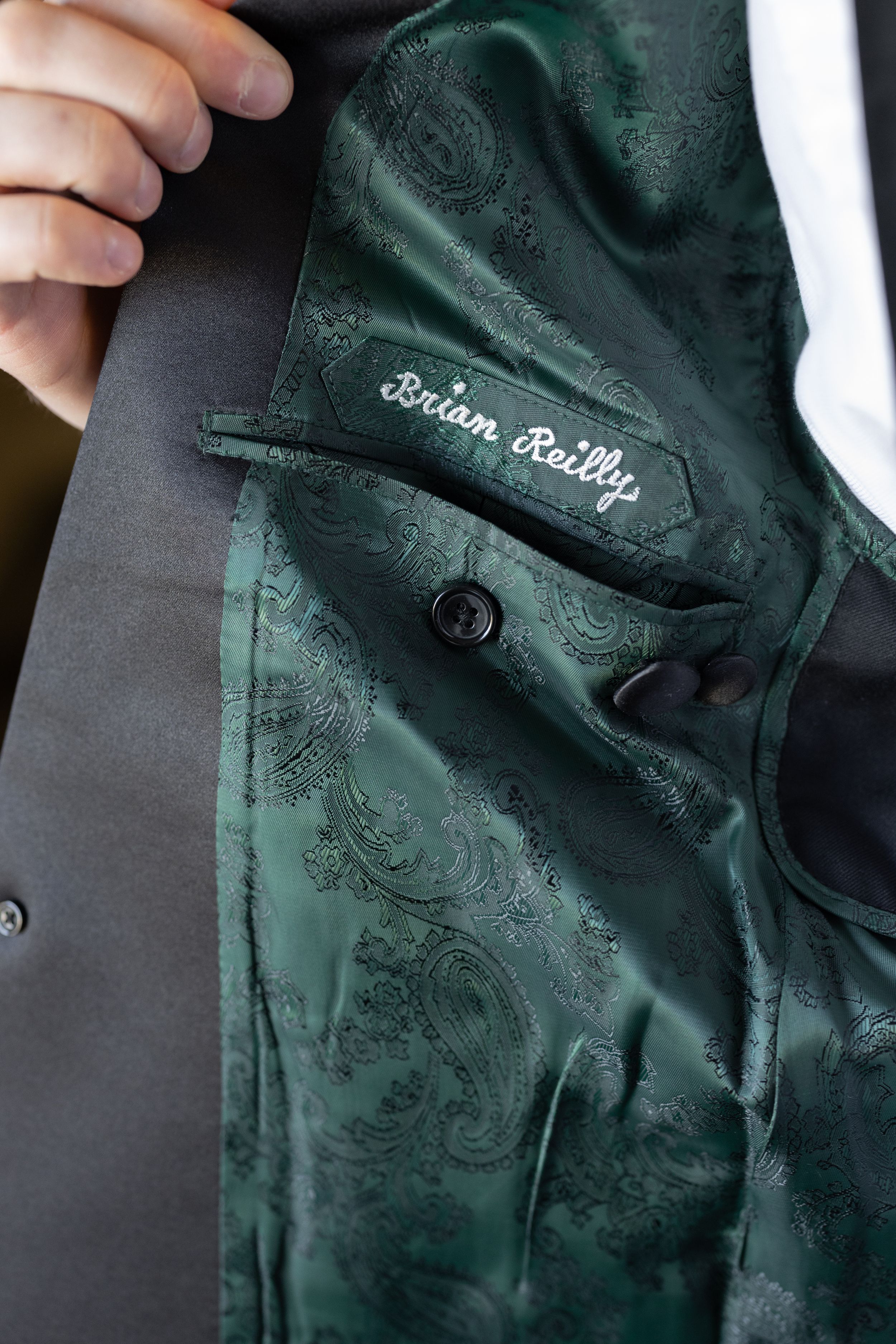 Custom green paisley suit lining with embroidered name tag reading Brian Reilly on a tailored gray jacket.