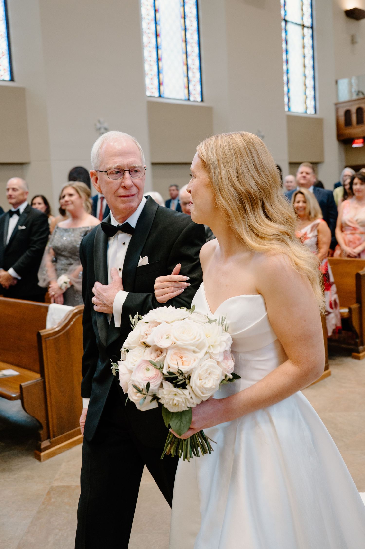 Bride holding white rose bouquet walks down church aisle with father in tuxedo during wedding ceremony in Cincinnati by K Herman Photography