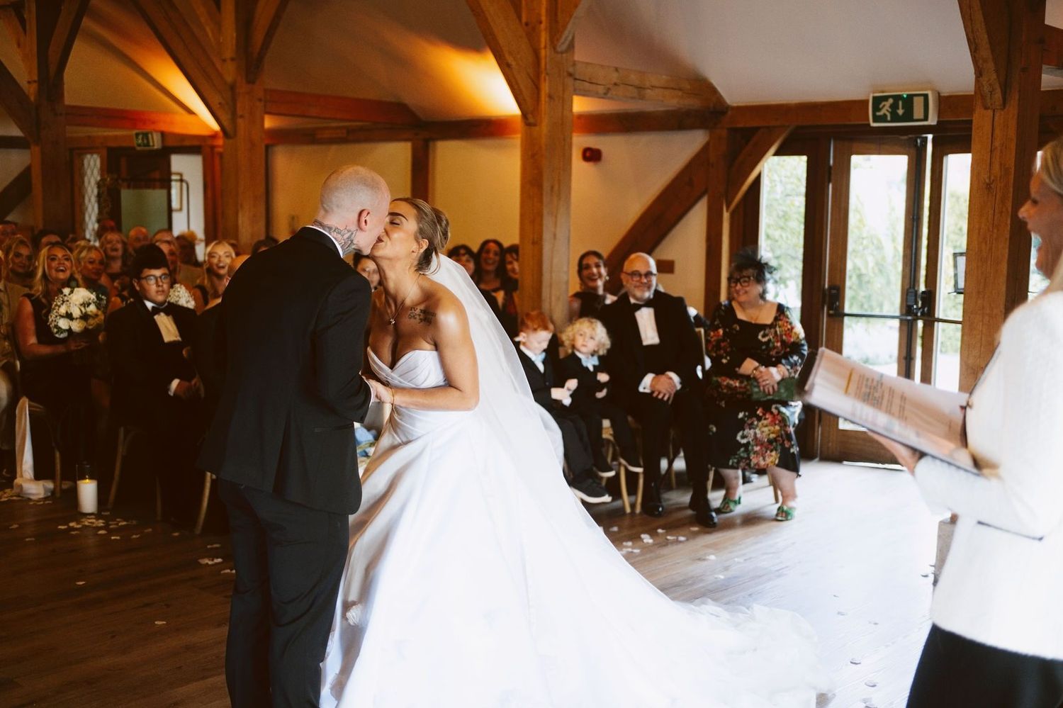 Bride and groom kiss at the front of the Ceremony Barn at Sandhole Oak Barn as smiling guests look on