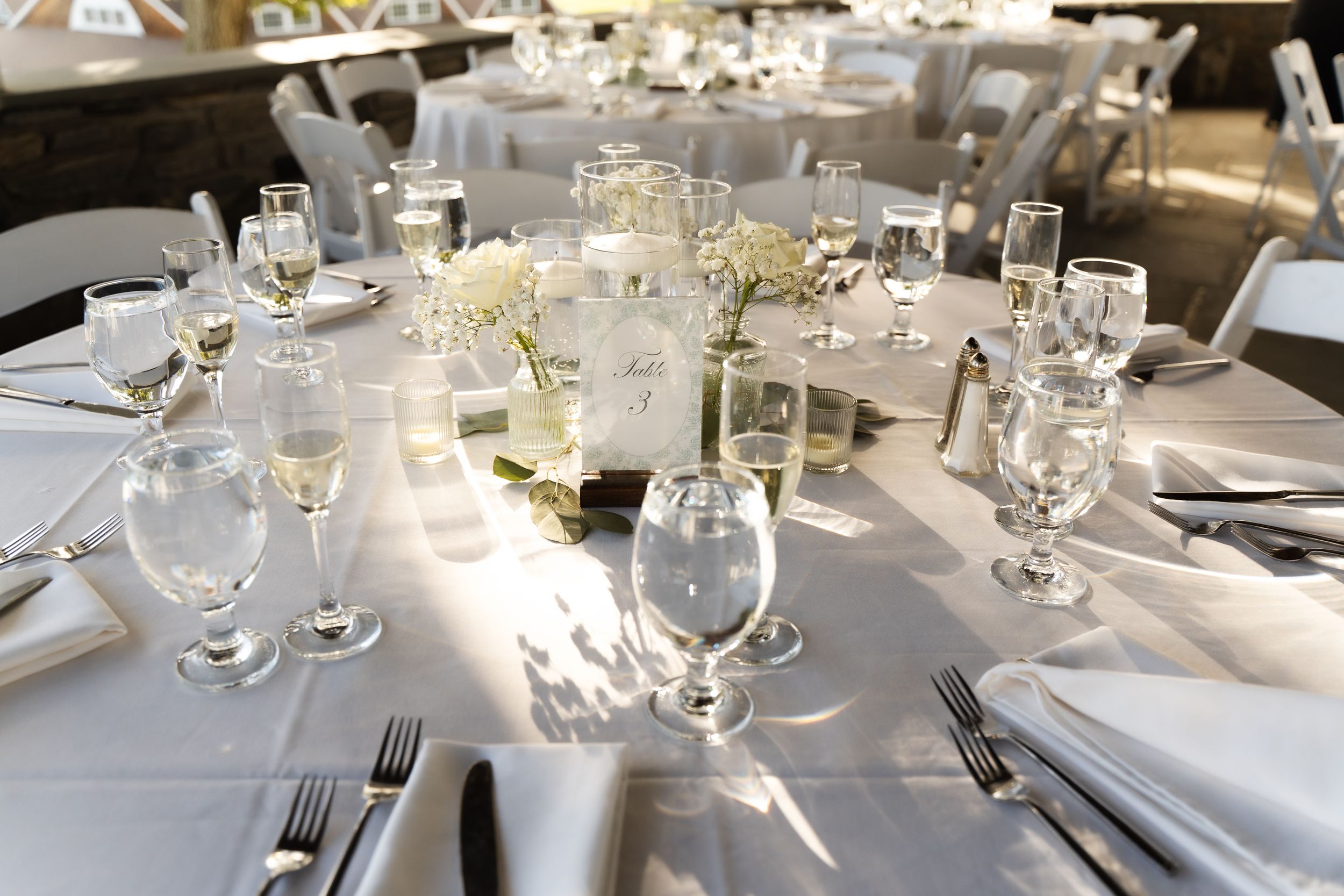 Elegant wedding reception table set with white linens, crystal glassware, silverware, and floral centerpieces.