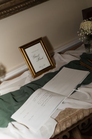 Elegant wedding guest book display with gold frame, open book, and green satin ribbon on a decorated table.
