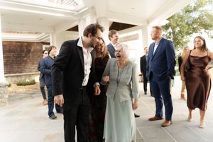 Elegantly dressed guests mingle outdoors at a formal event, with an older woman in mint green being greeted warmly.