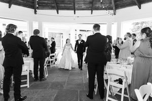 Bride and groom make grand entrance into elegant wedding reception hall while guests applaud and celebrate.