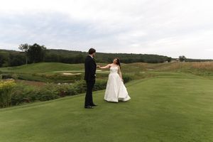 Bride and groom hold hands dancing on green golf course fairway with rolling hills on their wedding day.