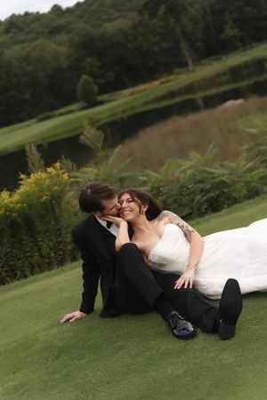 Happy bride and groom sitting on lush green grass, sharing a romantic moment at their outdoor wedding.