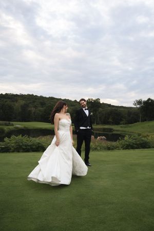 Bride in strapless white gown and groom in black tuxedo walking on a green golf course at their wedding.