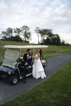 Bride and groom share champagne beside a golf cart on a scenic course path at dusk.