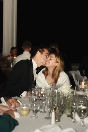 Couple sharing a romantic kiss at a candlelit wedding reception dinner table with elegant glassware.