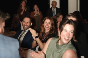 Guests laughing and clapping at a formal event, seated at tables in an elegant venue.