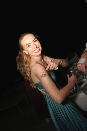 Smiling woman in teal dress with shoulder tattoo at a nighttime event.