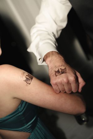 Matching cat tattoos on a couple's wrist and leg, showcasing fine line portrait ink art.