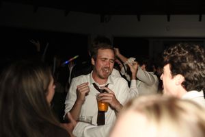 Man dancing at a party holding a beer bottle, surrounded by crowd in dimly lit venue.