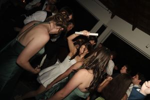 Wedding guests dancing together in dimly lit reception venue wearing formal attire.