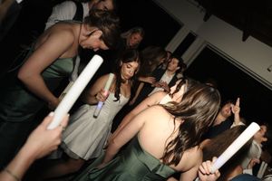 Wedding guests in green bridesmaid dresses dancing with white glow sticks at a nighttime reception.