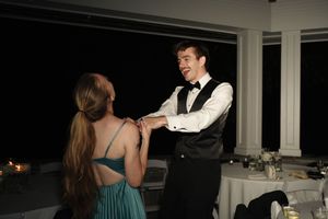 Smiling groom in bow tie and vest holding hands with guest in teal dress at wedding reception.