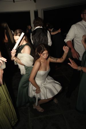 Bride in short white dress dances energetically with guests at lively wedding reception party.