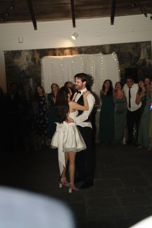 Couple shares romantic first dance embracing on dance floor while wedding guests watch and celebrate.