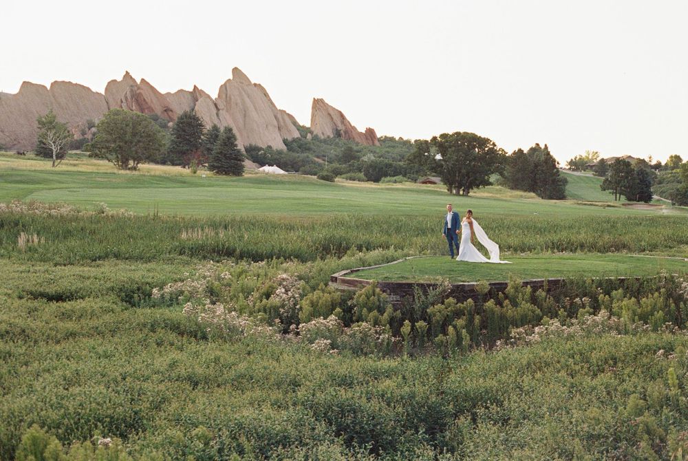 Bride and groom stand together on a green golf course with red sandstone rock formations rising in the background under a soft hazy sky.