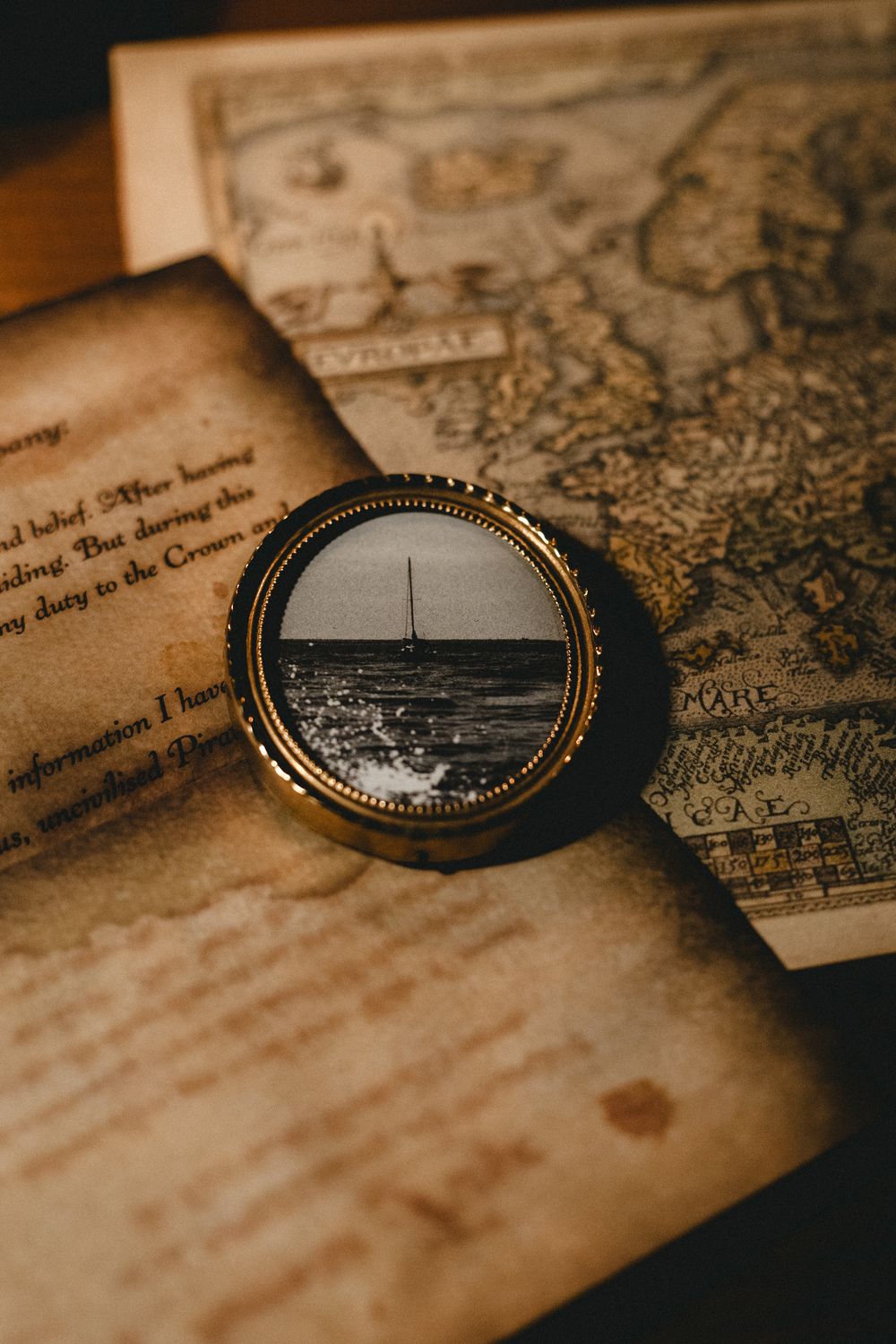 Vintage compass with sailboat reflection resting on aged antique map and handwritten letter.
