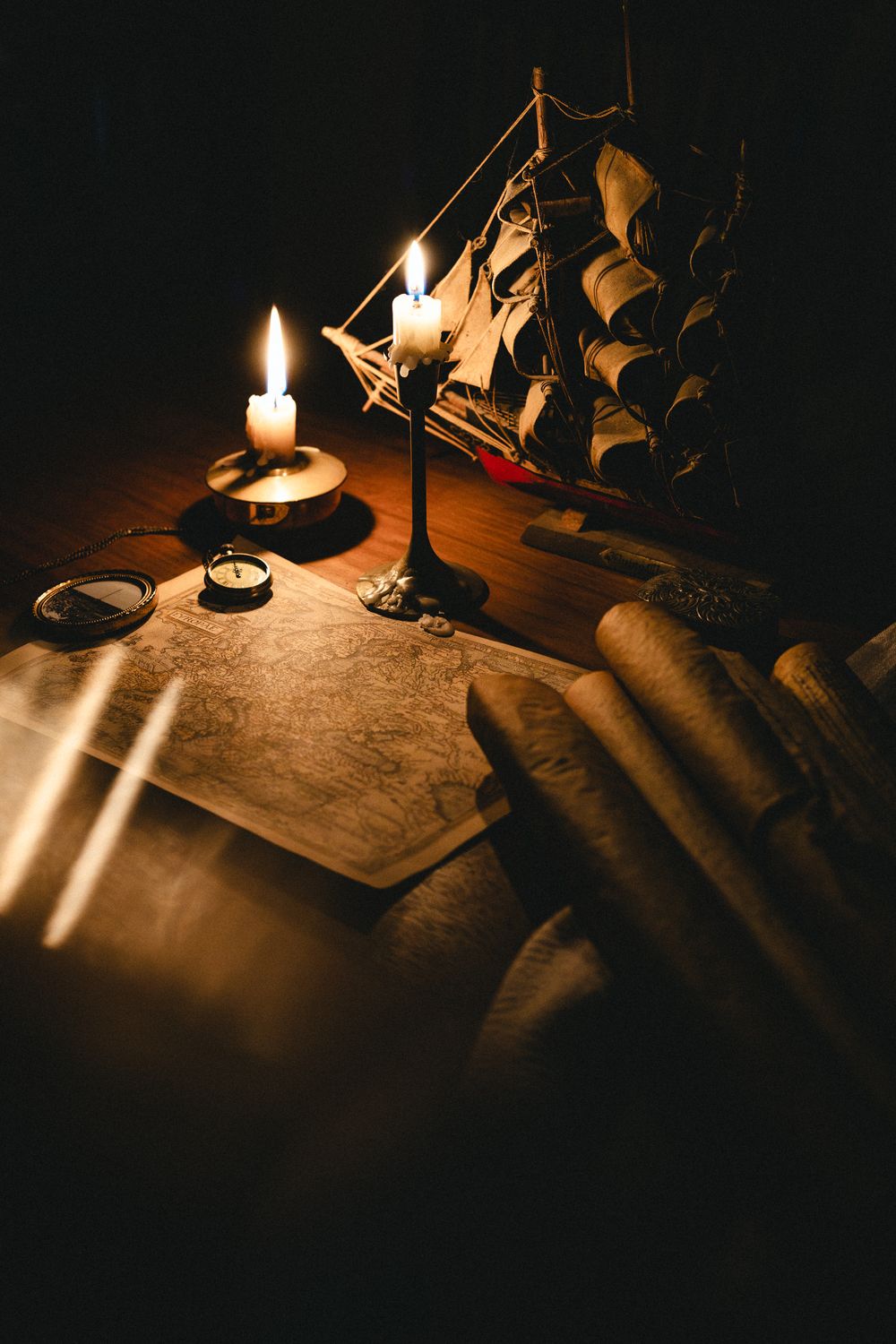Vintage nautical map with compass, scrolls, lit candles, and a model sailing ship on a wooden table in candlelight.