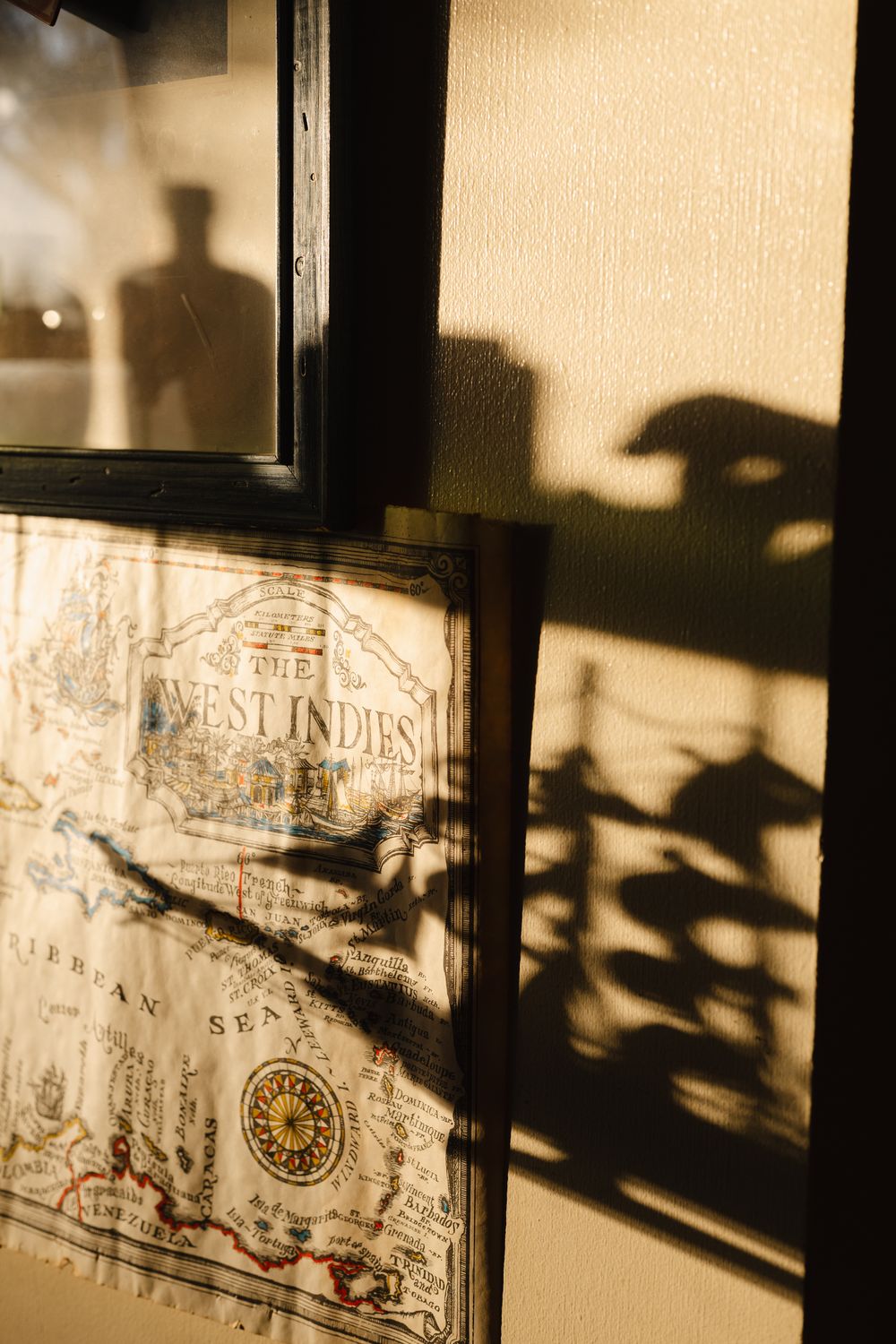 Vintage West Indies map framed on wall with dramatic shadows and warm golden light creating atmospheric decor.