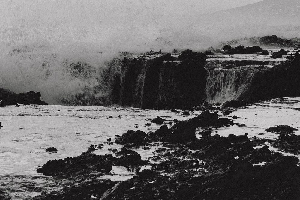 Black and white photo of a powerful waterfall cascading over rocky cliffs into a turbulent river below.
