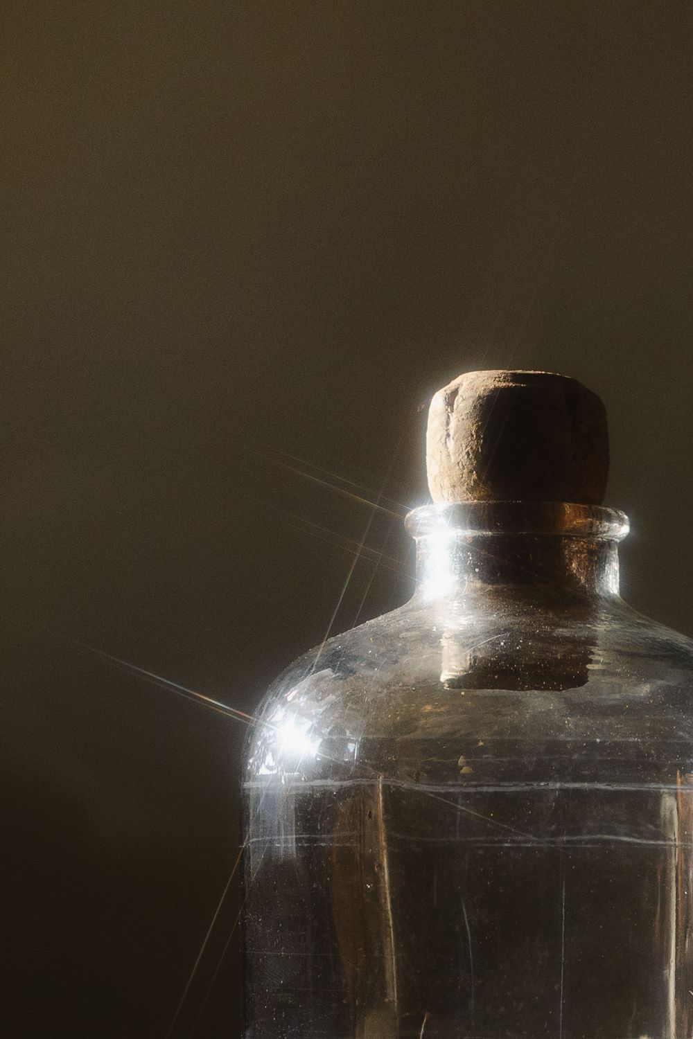 Antique glass bottle with cork stopper and spider webs, illuminated by dramatic light on dark background.