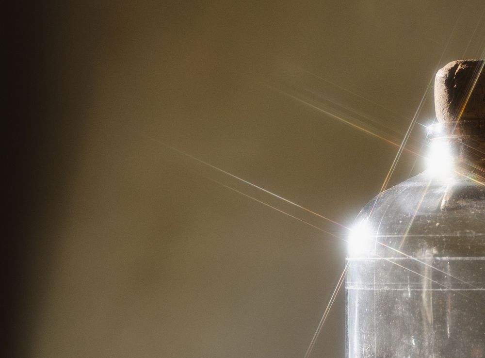 Close-up of a glass bottle with light refracting through it, creating bright star-burst rays on a warm background.