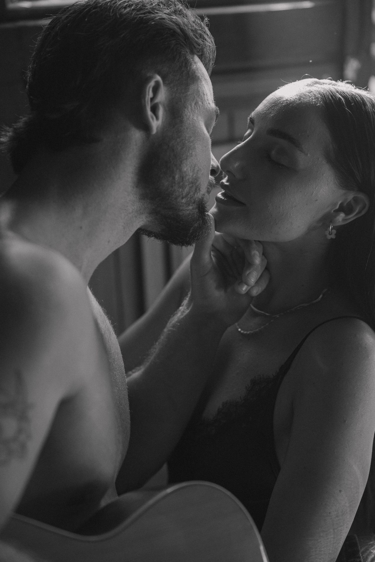 Intimate black and white close-up of a couple about to kiss, with an acoustic guitar visible in the foreground.