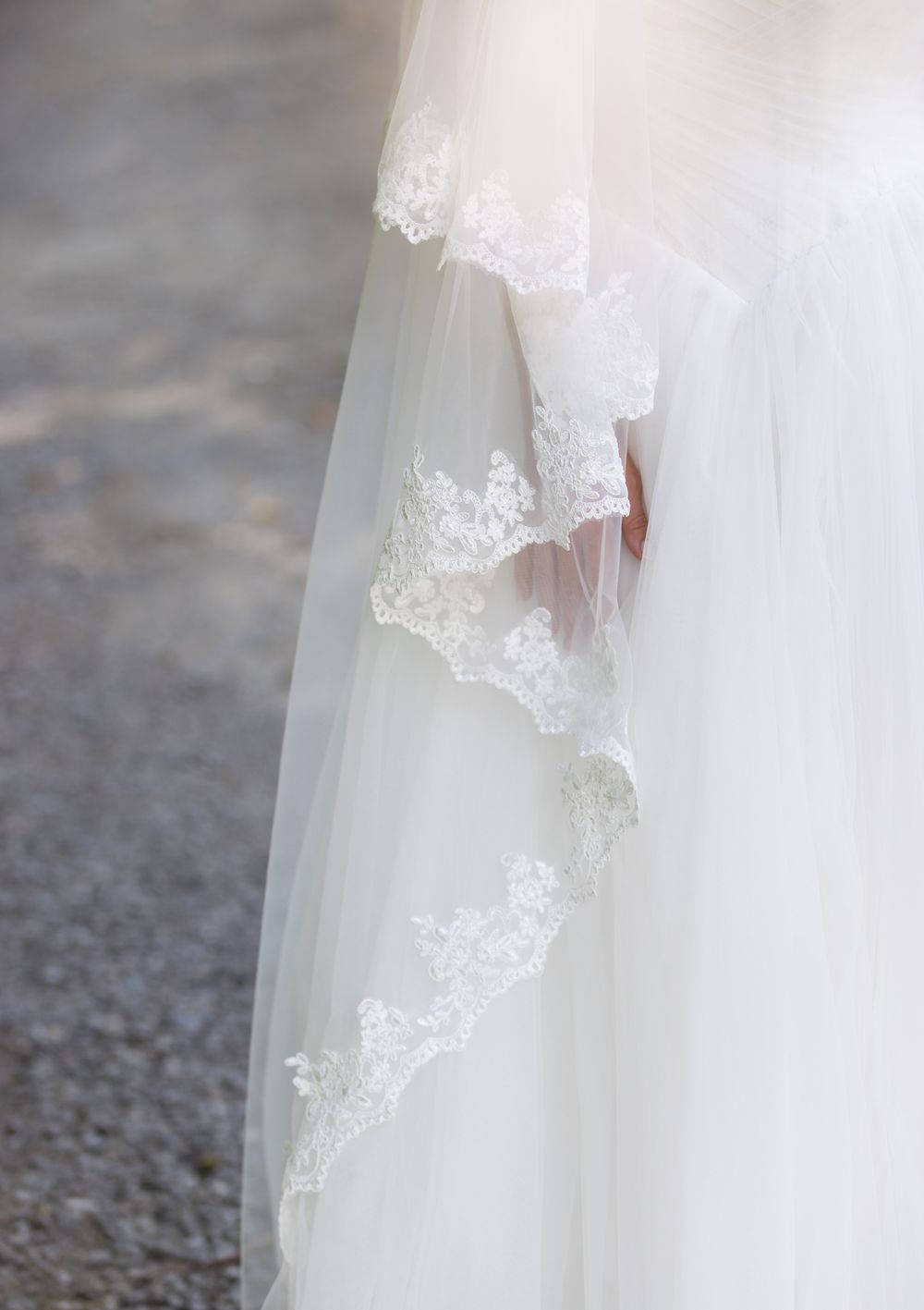 Close up of bride's hand peeking through white tulle gown with delicate lace-trimmed veil. Concord Groton wedding photographer.