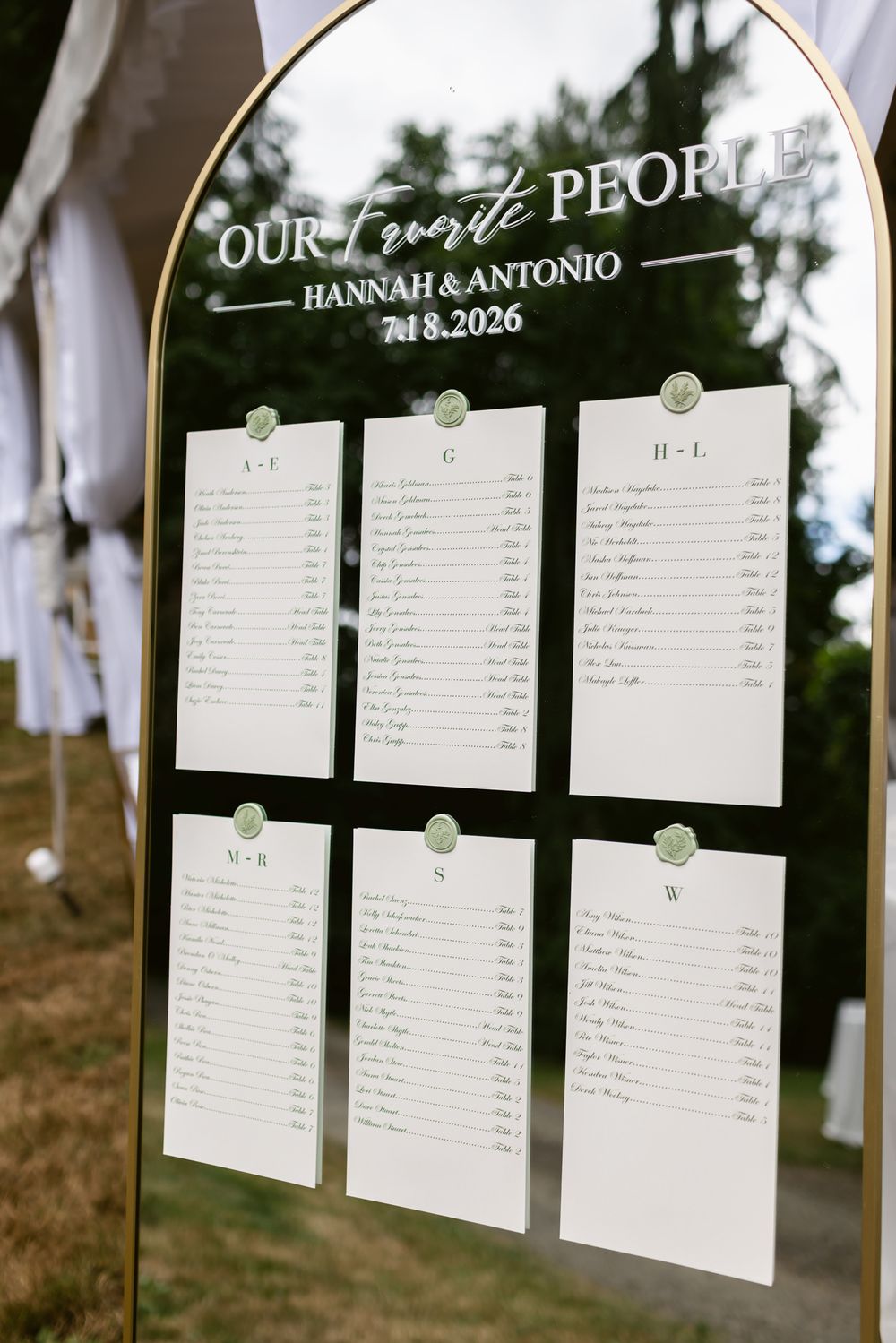 Arched gold framed mirror seating chart outdoors reading Our Favorite People with six alphabetical guest lists. Rye wedding photographer