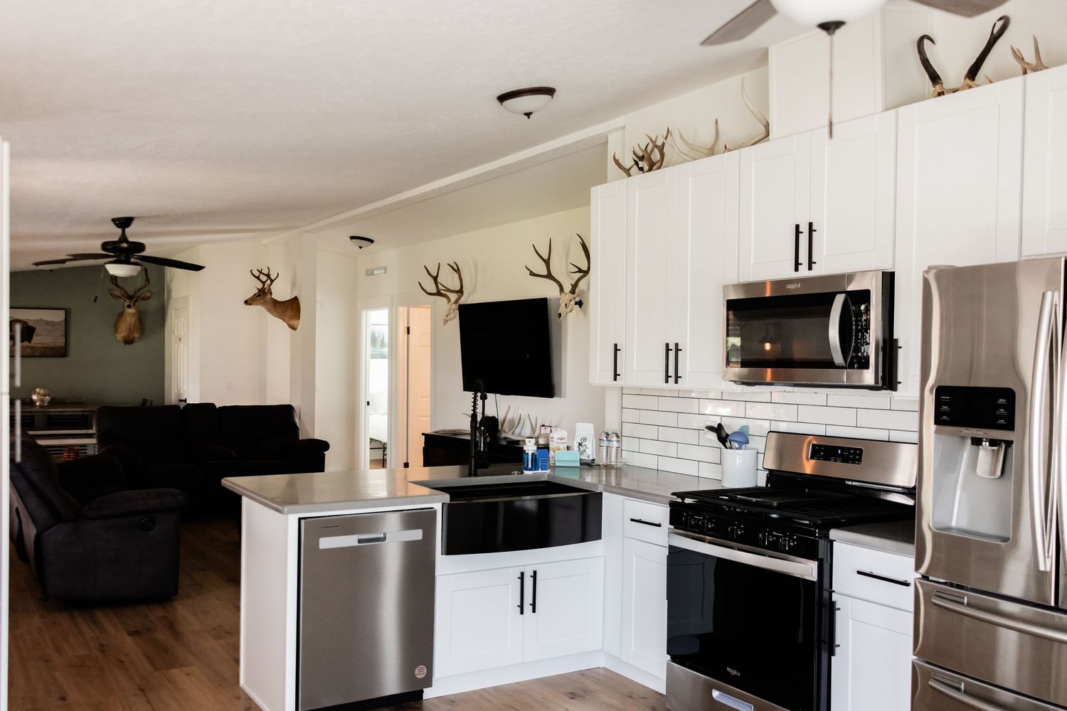 Open-concept kitchen with white cabinets, stainless steel appliances, a breakfast bar, and antler decor leading to a cozy living room.